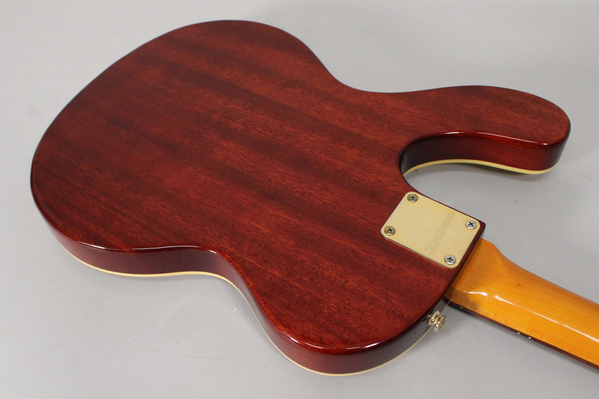 The guitar's back is a rich reddish-brown with visible wood grain, a cream binding, and a gold neck plate with four screws.