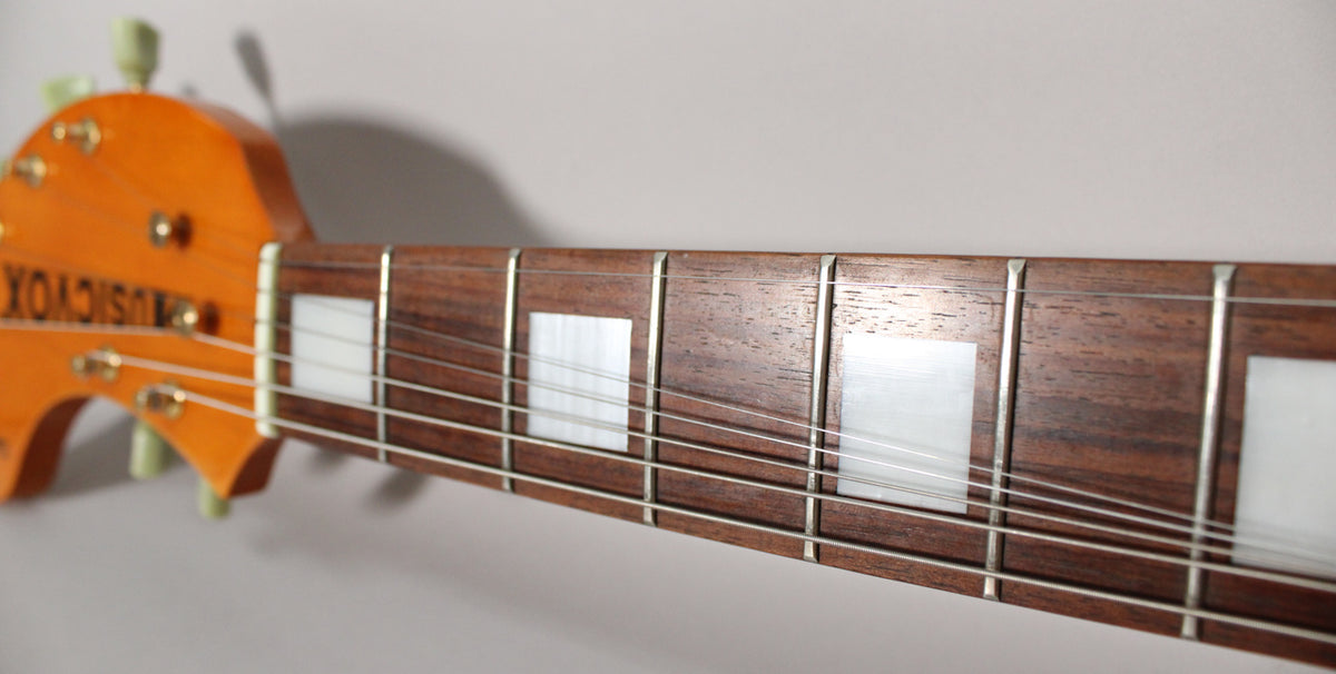 Close-up of the guitar's dark fretboard with rectangular white block inlays, showing the headstock and tuning pegs on the left.