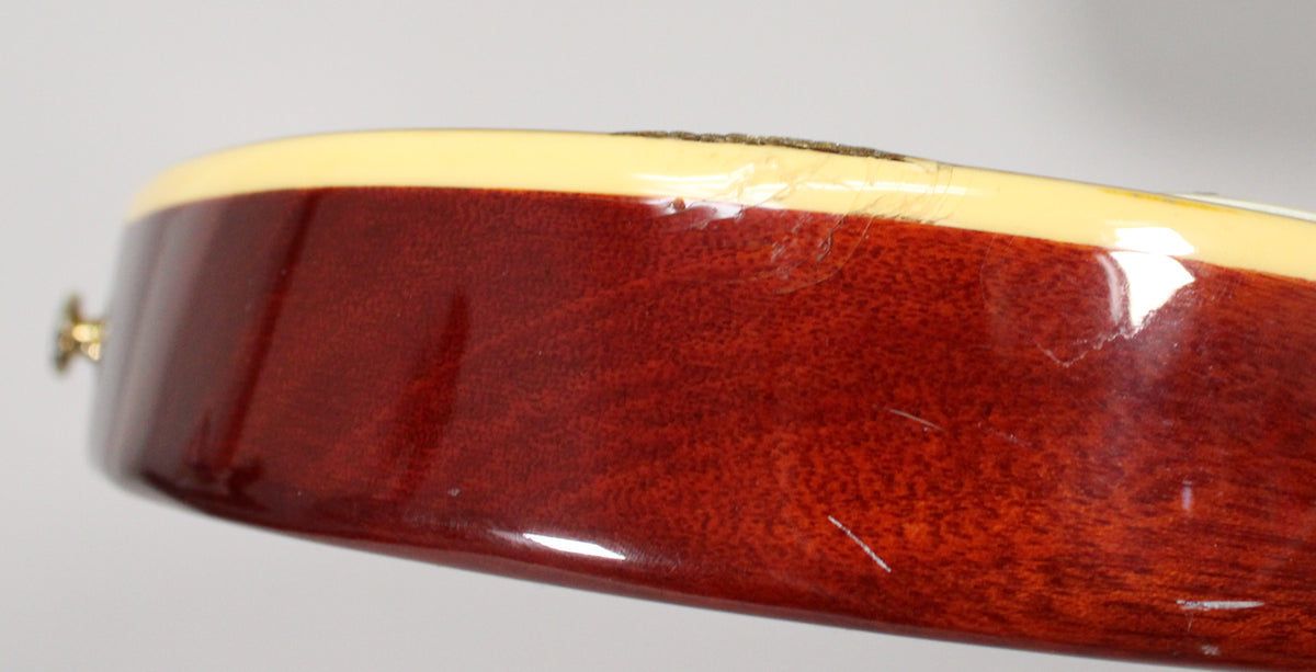 Close-up of the guitar's lower bout, showing the dark red wood grain, cream binding, and several scratches and finish checking.
