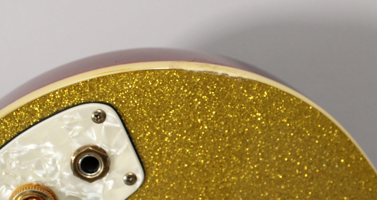 Close-up of the guitar's gold sparkle finish, showing the output jack on a pearloid plate and binding wear on the upper edge.