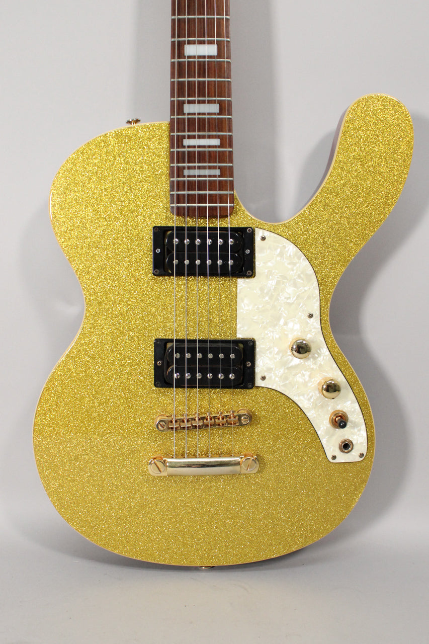 The gold sparkle guitar body is framed from the neck joint down, showing two black humbuckers and a pearloid pickguard.