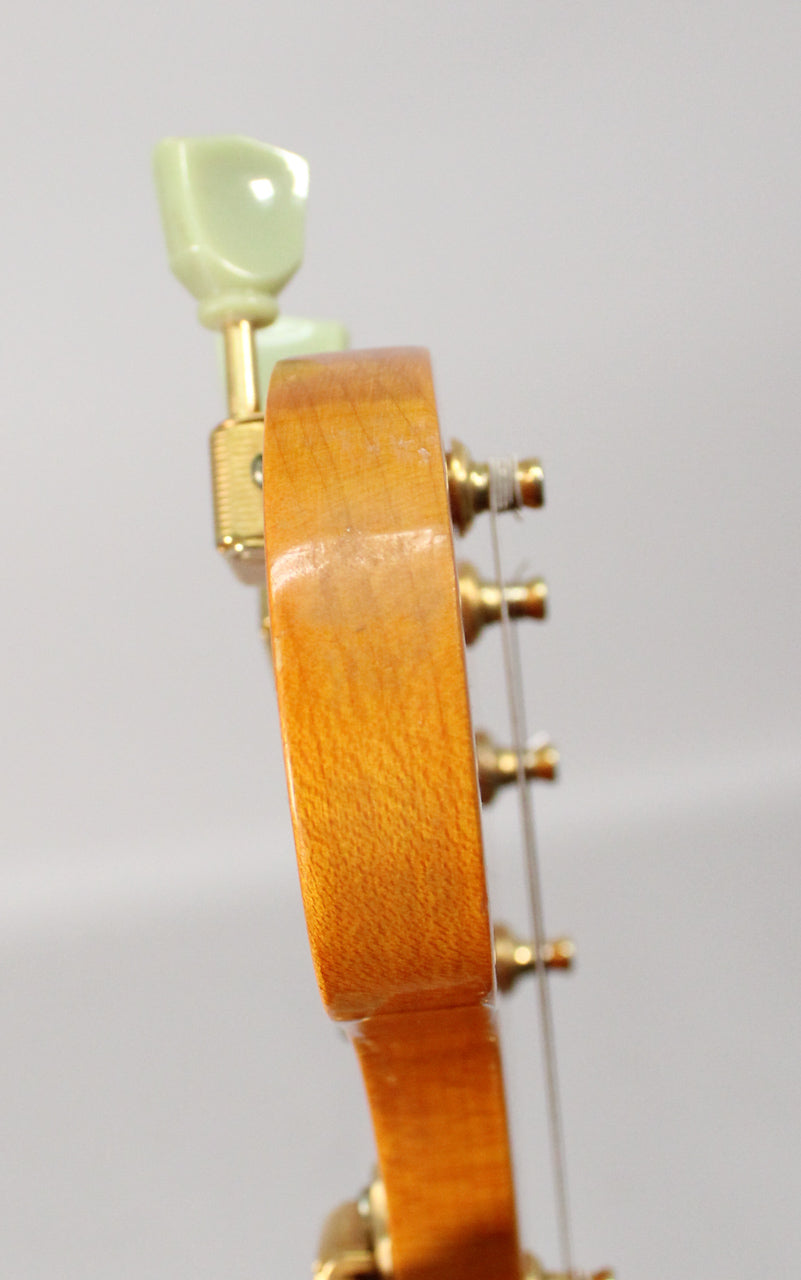Close-up side view of the guitar's headstock, showing a light brown wood finish, gold tuners with pale green buttons, and light wear.