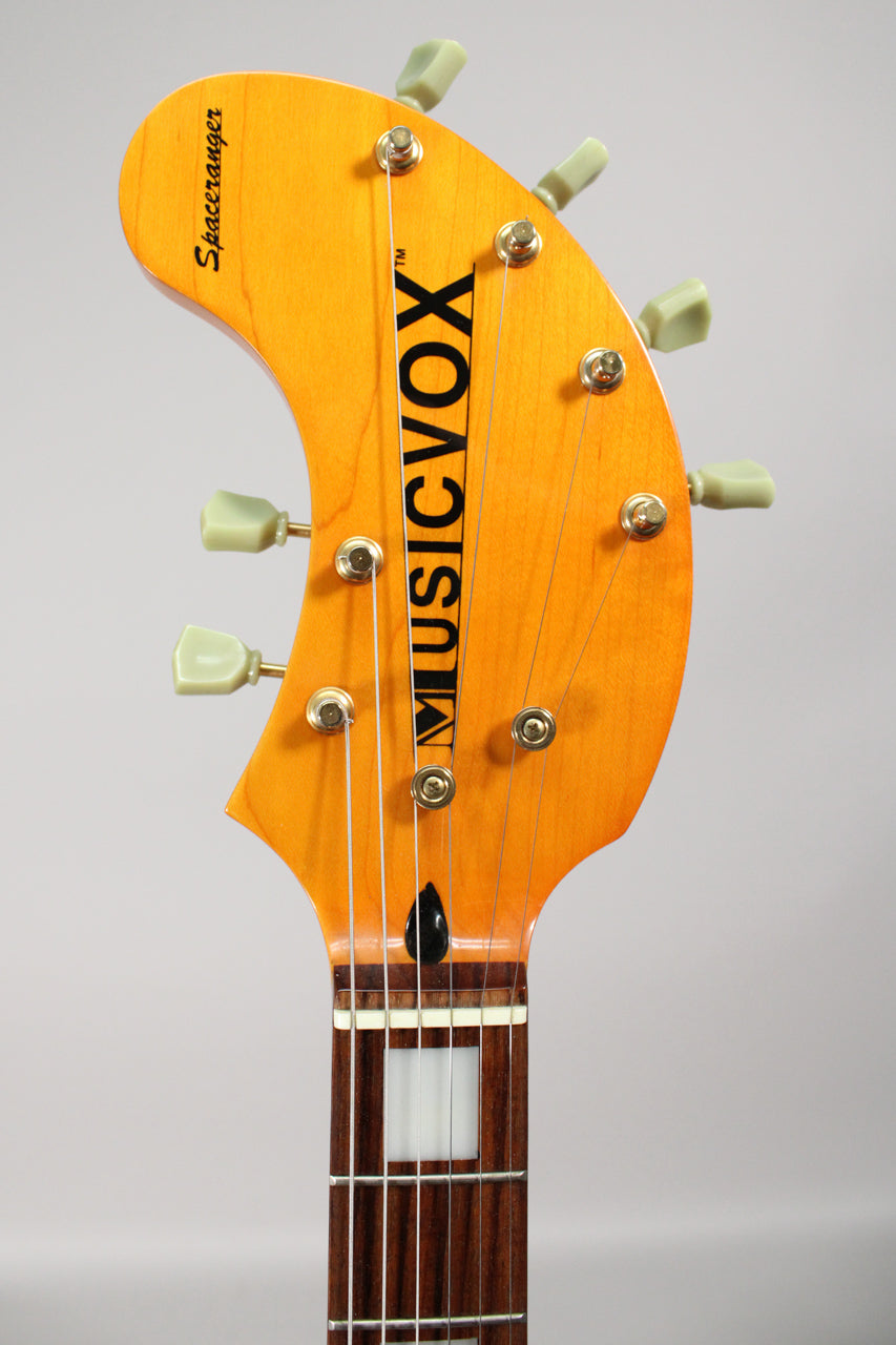 The guitar's light brown headstock, with six pale green tuners and gold hardware, is angled slightly left, showing the top of the dark fretboard.
