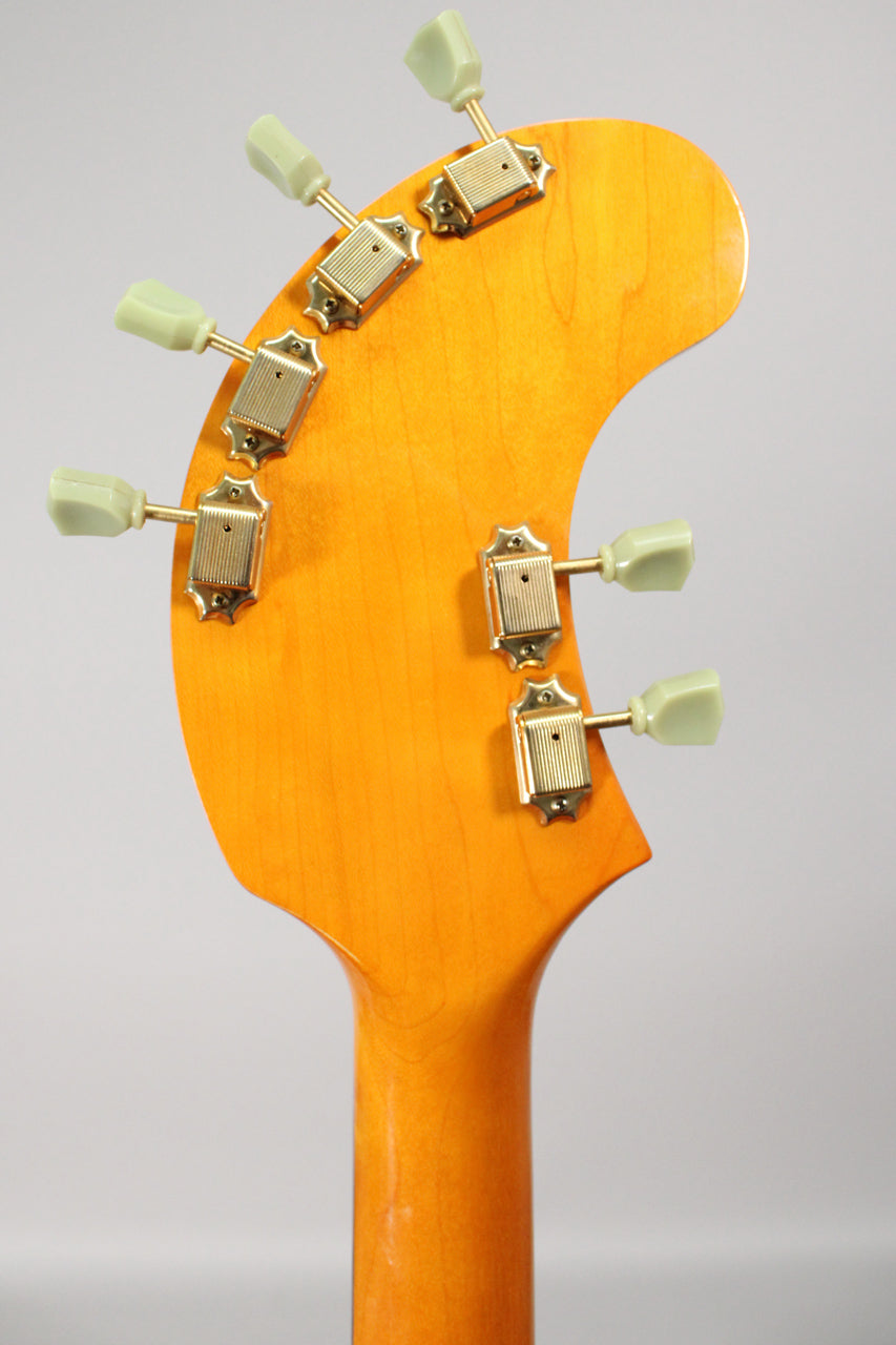 The guitar's headstock, viewed from the back, shows six gold-plated tuners with ribbed casings and light green plastic buttons.