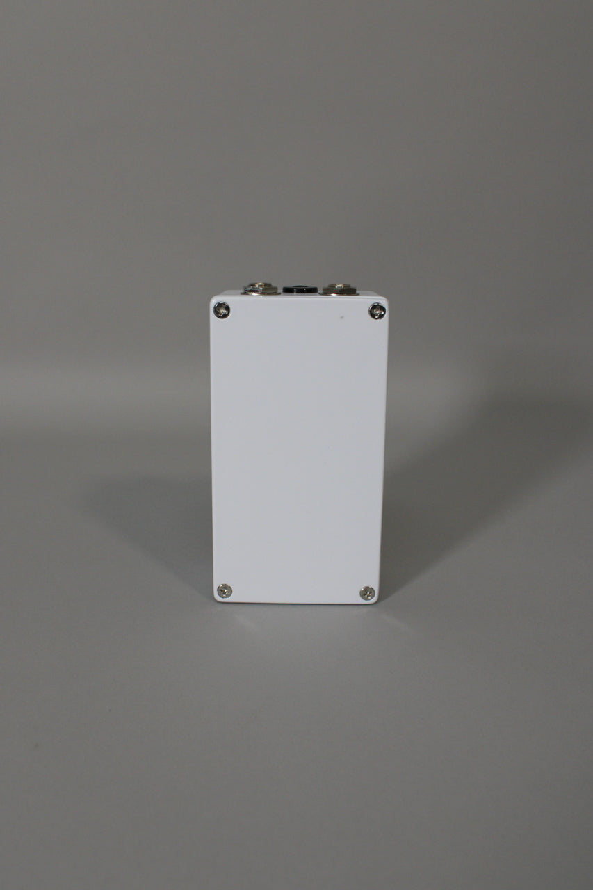 The white pedal is viewed from the back, showing two silver jacks and a black power input on the top edge.