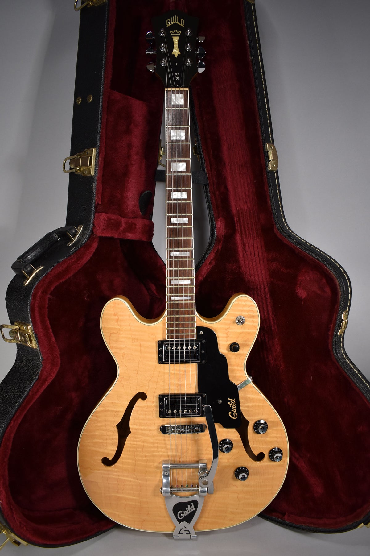 Full-length view of a natural finish hollow-body electric guitar with f-holes, a black pickguard, two humbuckers, and a Bigsby vibrato.