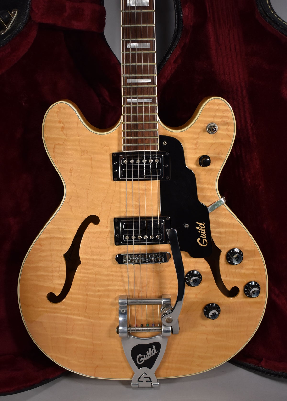 Full-body view of a natural finish hollow-body electric guitar with a Bigsby vibrato, two humbuckers, and a black pickguard.