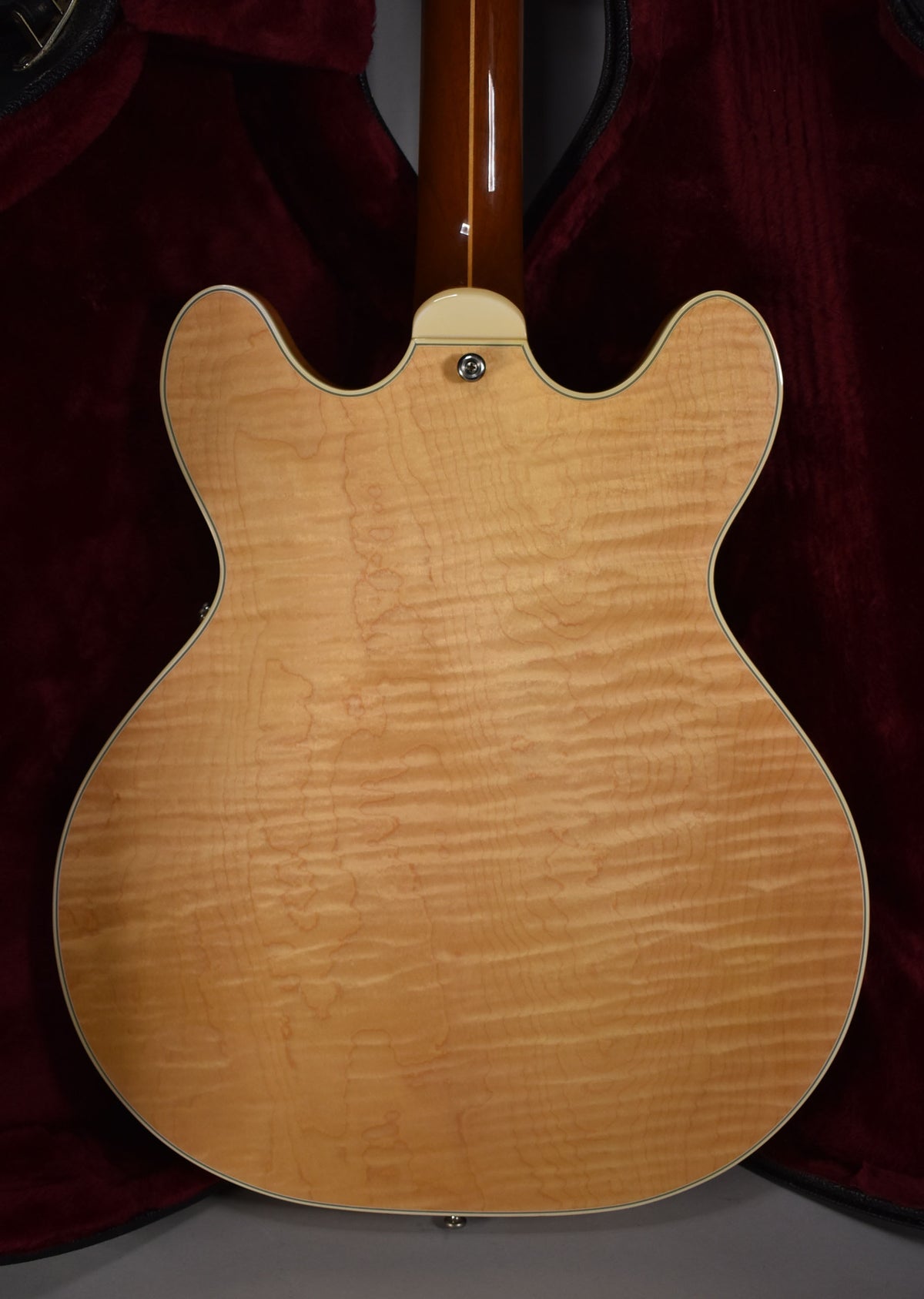 The guitar's back, a natural flame maple finish, shows a chrome strap button and the neck heel with a dark brown neck.