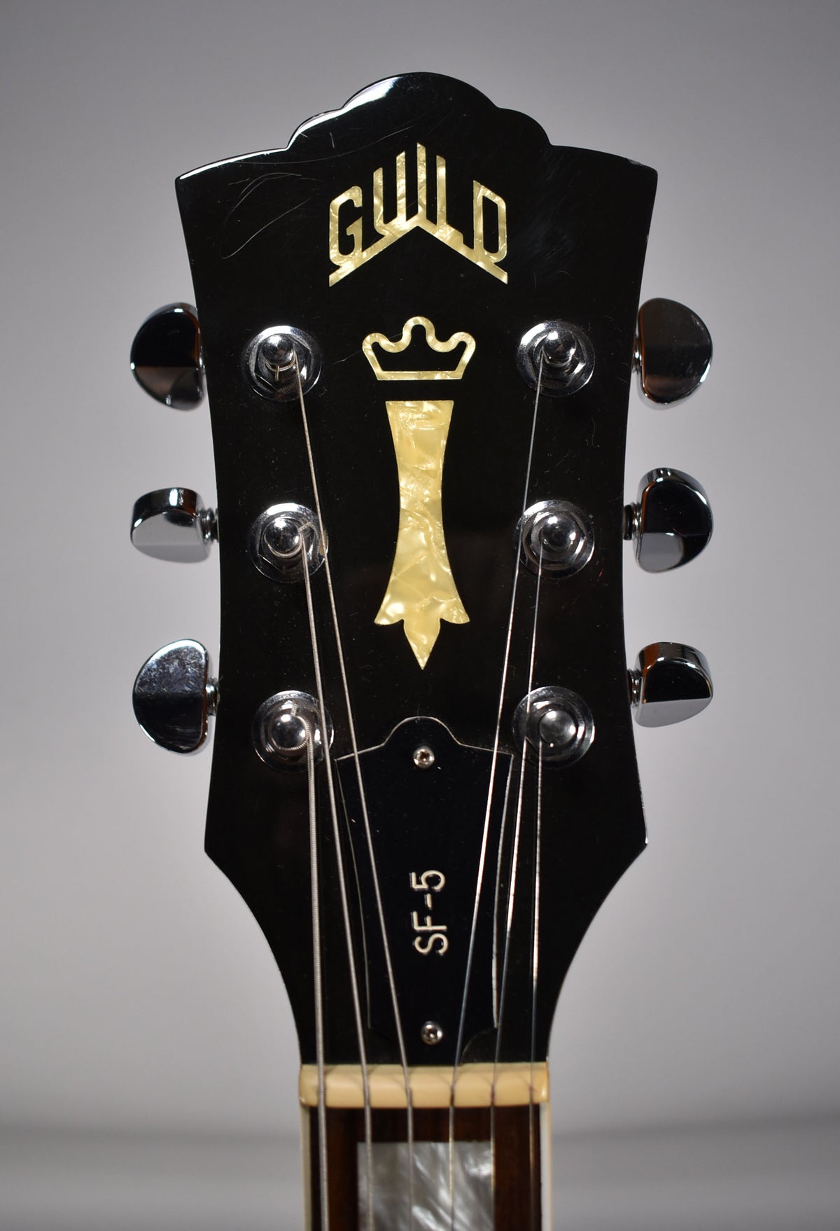 Close-up of a black gloss headstock with mother-of-pearl inlays, six chrome tuners, and light surface scratches.