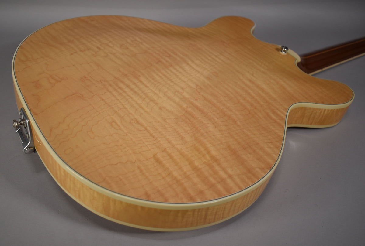 The guitar's back, angled from the lower bout, shows a natural flame maple finish with cream binding and a chrome strap button.