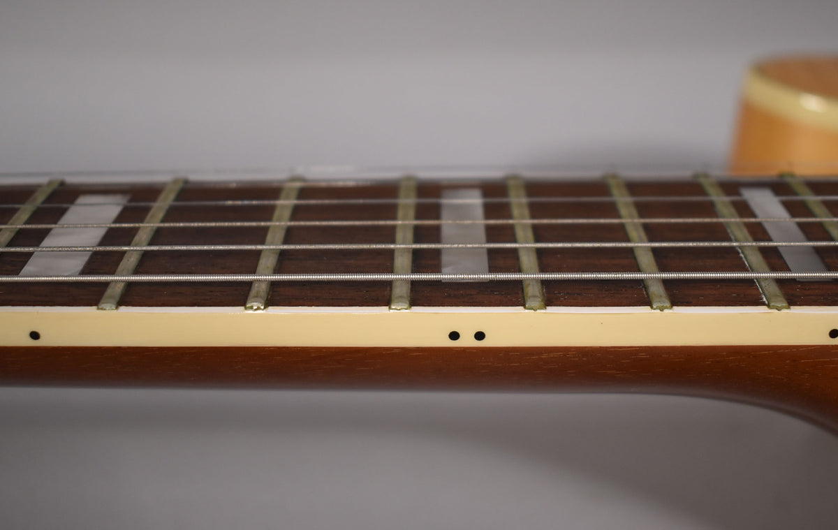 Close-up of the dark fretboard with rectangular inlays and side dots, showing light wear on the frets and binding.