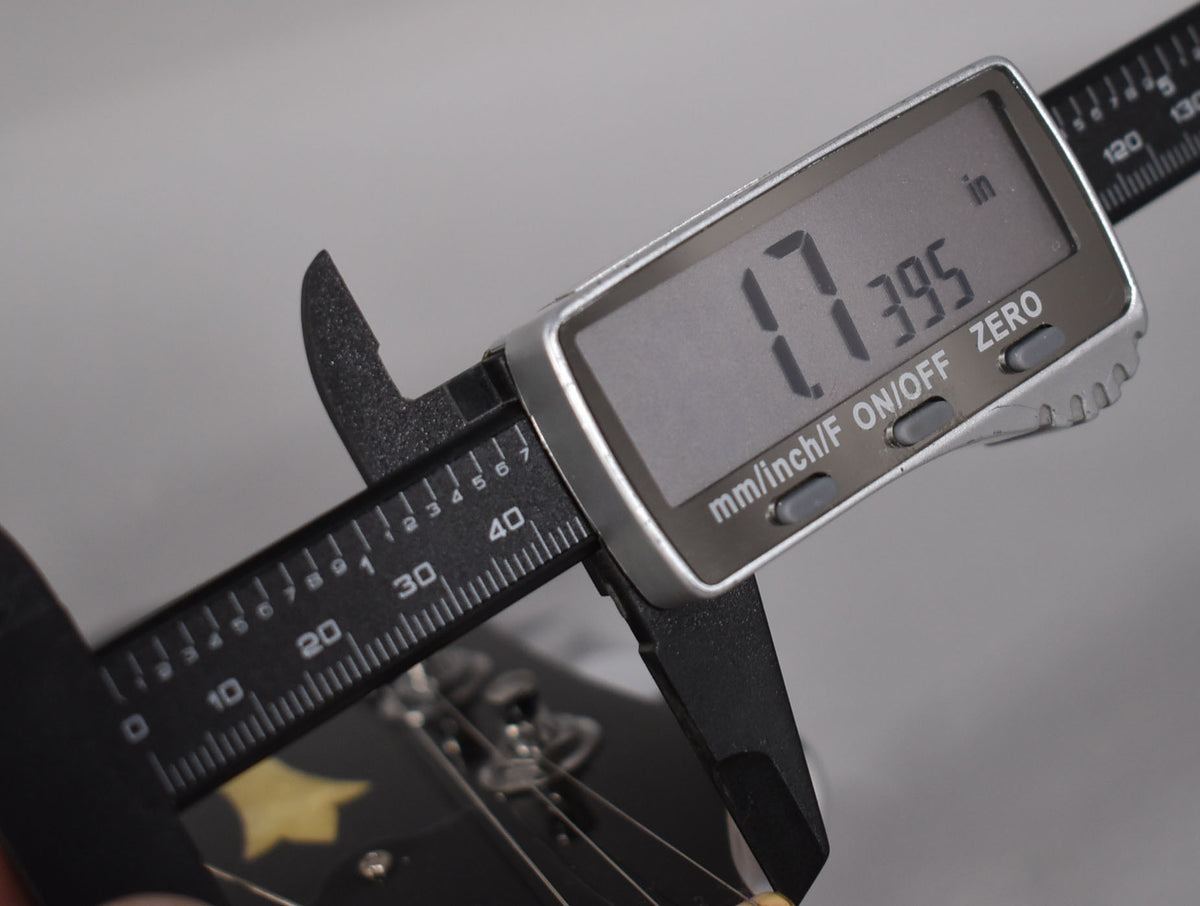 Close-up of a digital caliper measuring the nut width of the guitar's dark headstock, displaying "1.7395 in".