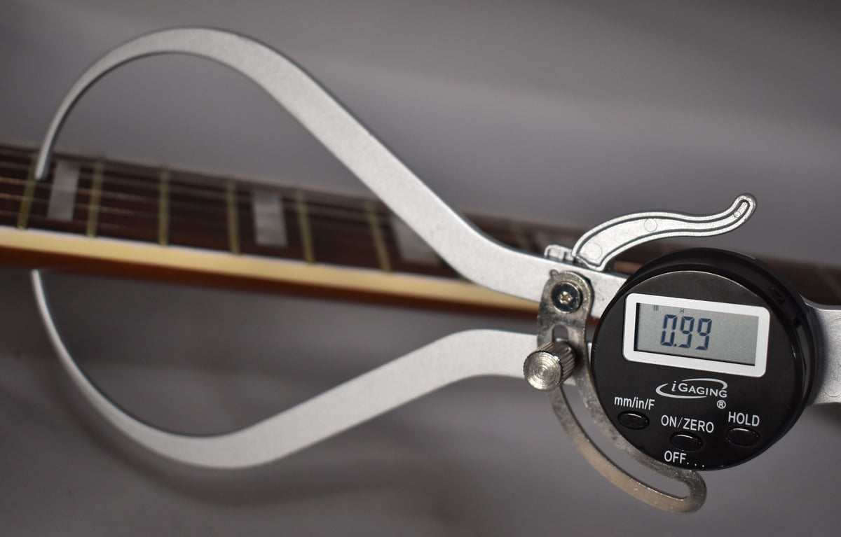 Close-up of the guitar's dark fretboard with rectangular inlays, measured at 0.99 by a silver digital caliper.