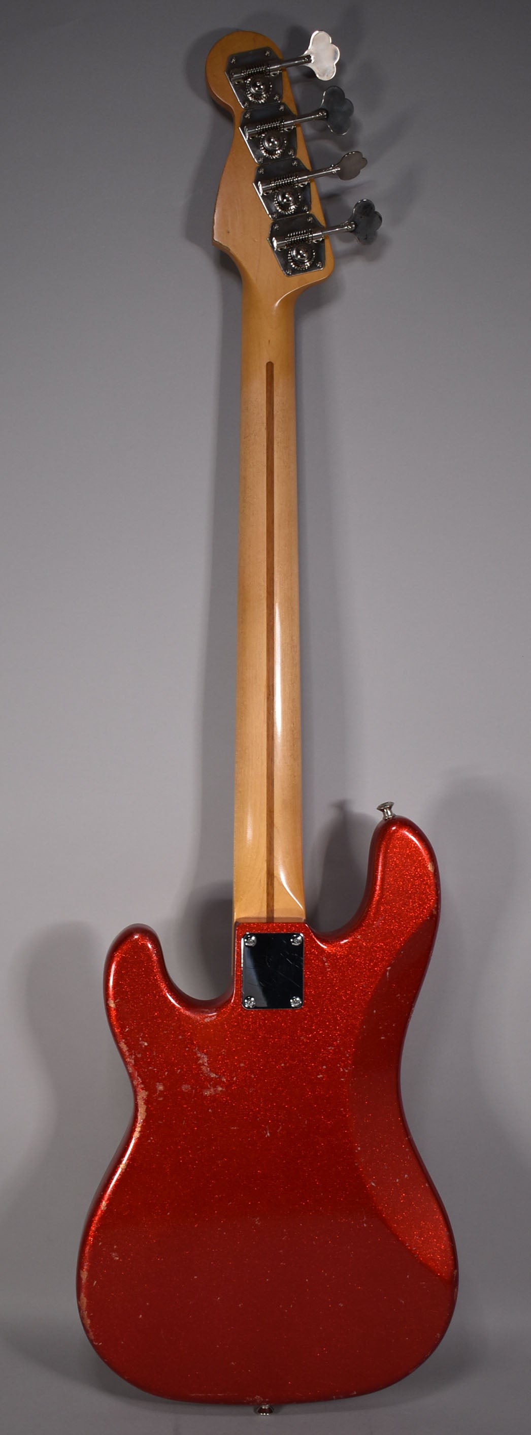 Full rear view of a red sparkle bass with a maple neck, showing heavy wear and checking on the body and a chrome neck plate.