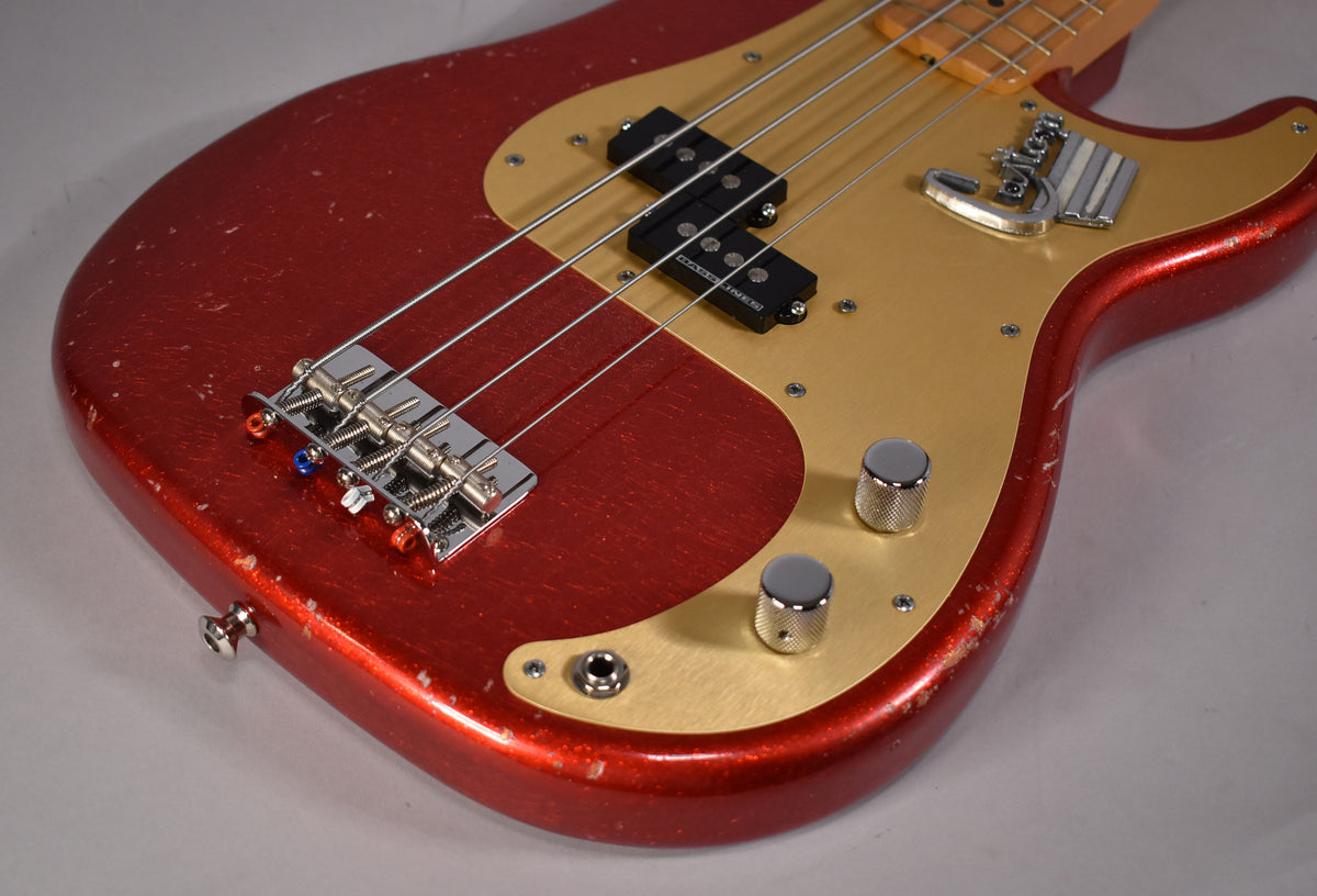 The aged red sparkle bass body, with a gold pickguard and chrome hardware, shows heavy finish wear and chipping.