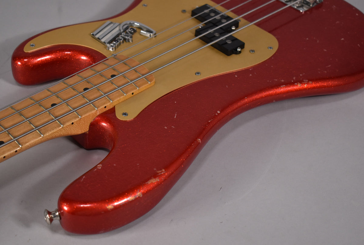 Close-up of the bass body, showing the red sparkle finish with heavy wear and chips, a gold pickguard, and a split-coil pickup.