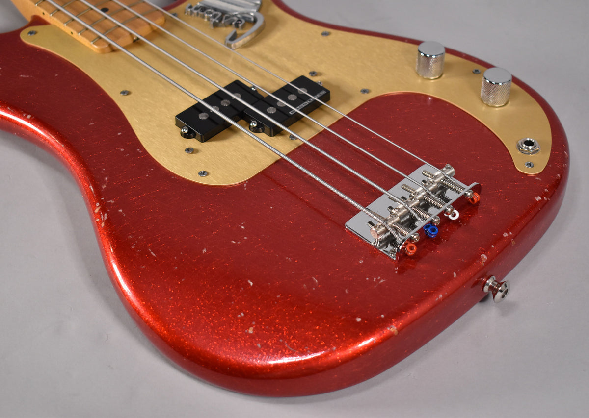 Close-up of a red sparkle bass body with a gold pickguard, showing a split pickup, chrome bridge, and heavy finish wear.