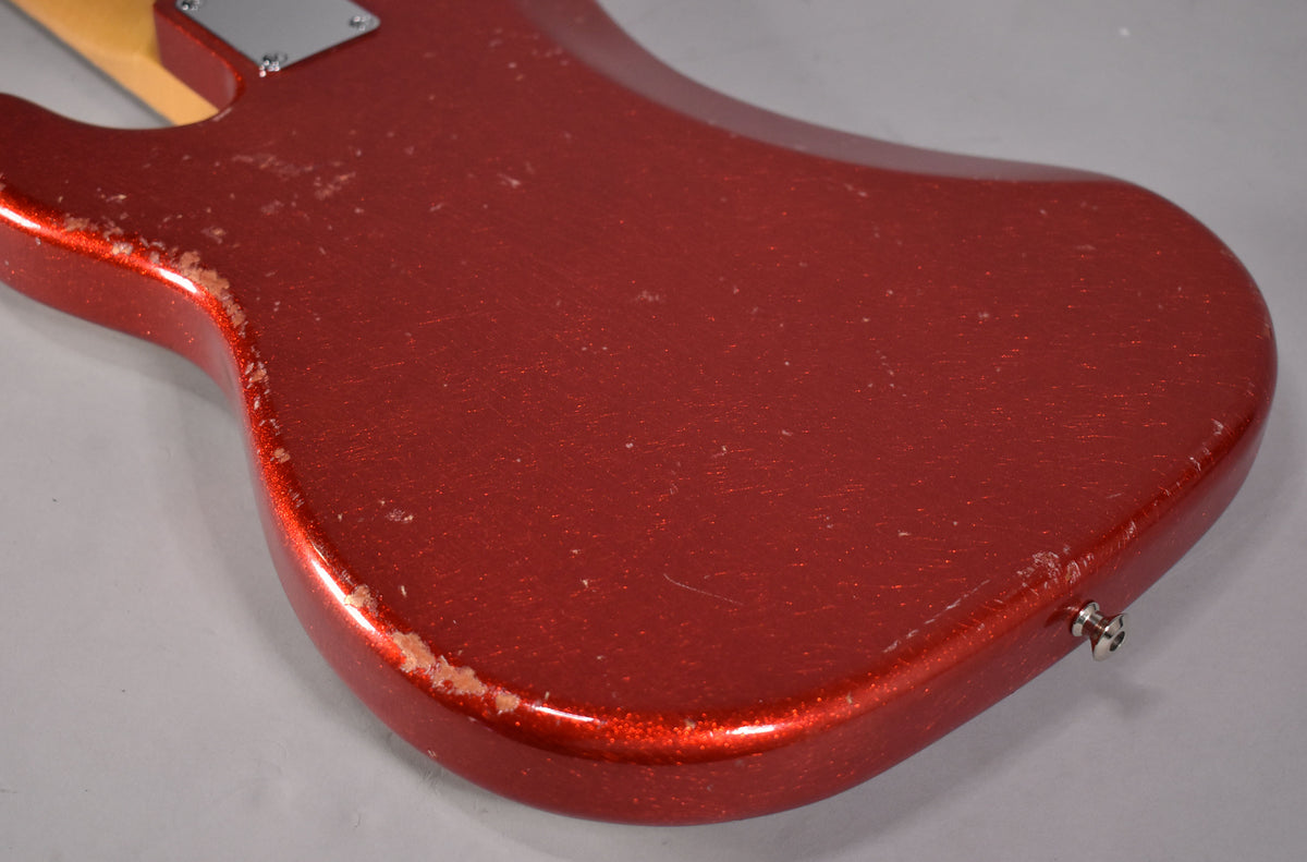 The bass's aged red sparkle body is shown from the back, with heavy wear and chipping along the lower edge and a visible output jack.