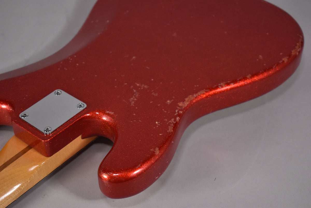 The bass's lower body, neck joint, and neck heel are visible, showing a red sparkle finish with heavy wear and chipping.