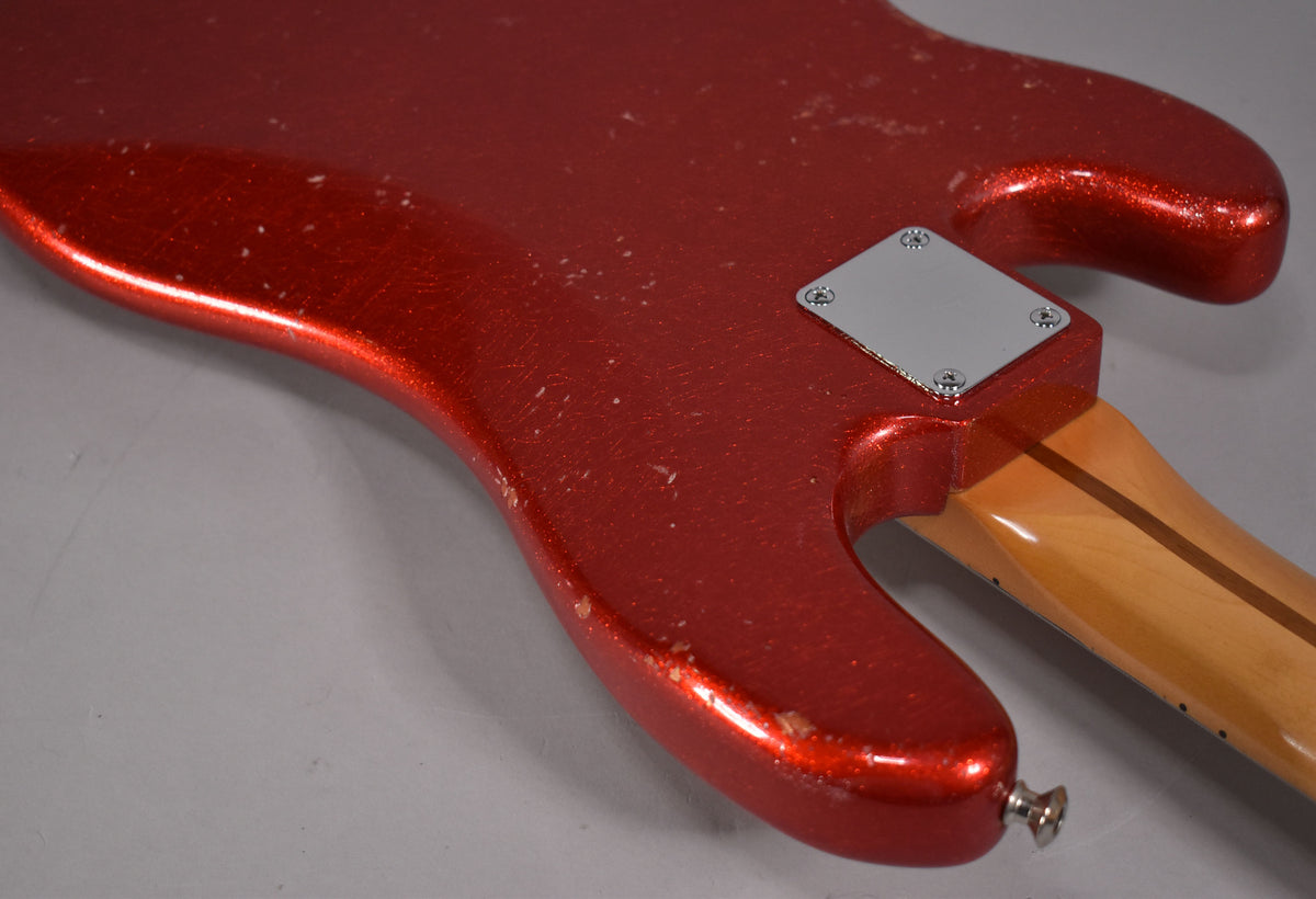 The bass's lower body, in aged red sparkle, shows heavy wear, chips, and scratches, with a chrome neck plate and strap button.