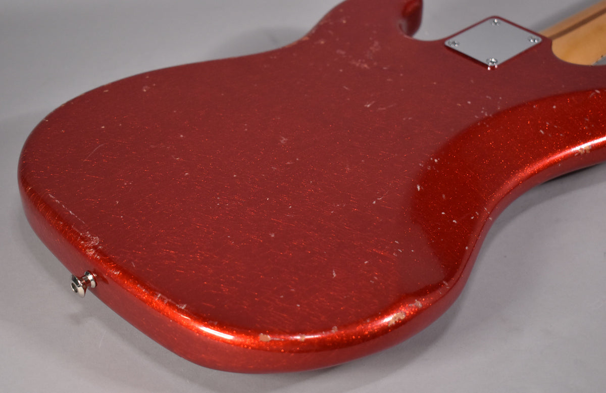 The back of the red sparkle bass body, angled from the lower left, shows heavy finish wear, scratches, and chips along the edges.