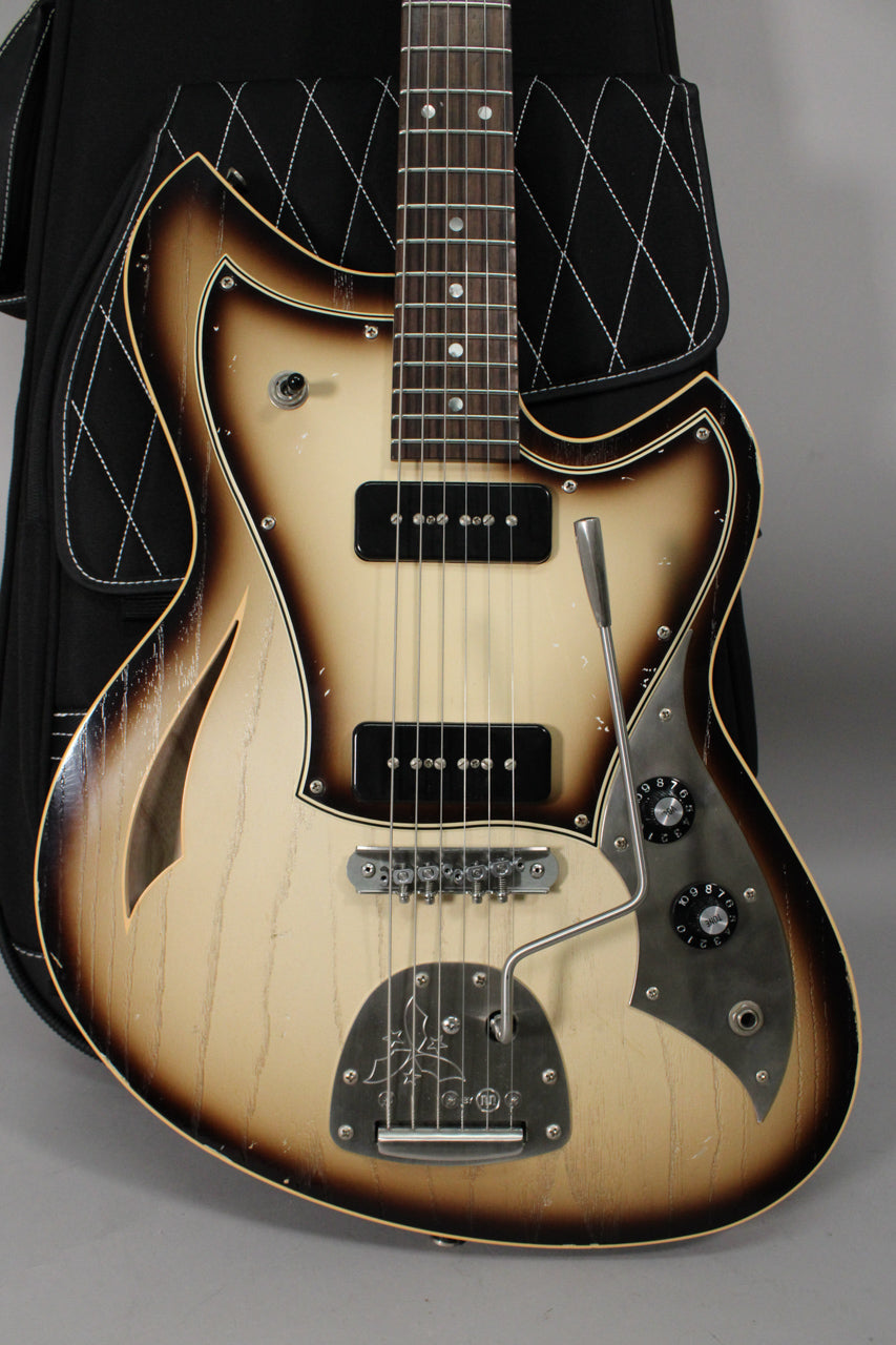 Full-frame view of a light-aged, cream and brown burst semi-hollow guitar with two P90 pickups, a vibrato, and f-holes.