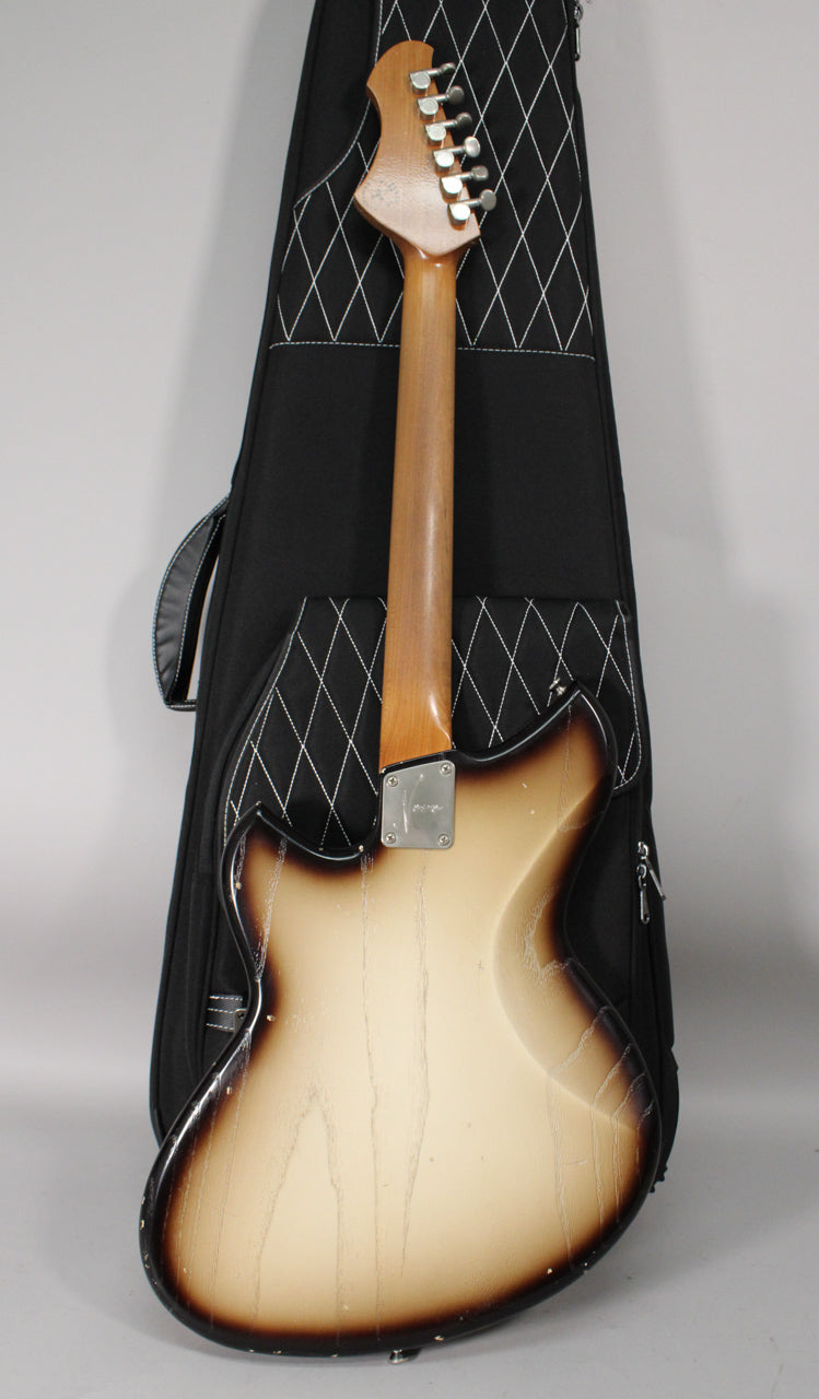The back of a light-aged, toasted marshmallow burst guitar with a maple neck and six inline tuners, resting in a black gig bag.