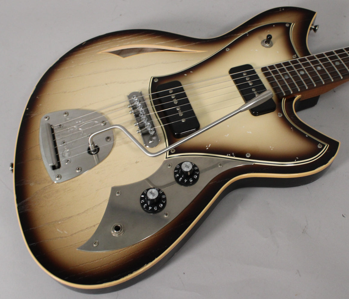 The semi-hollow guitar's body, with a toasted marshmallow burst finish and light aging, shows two P90 pickups and a tremolo arm.