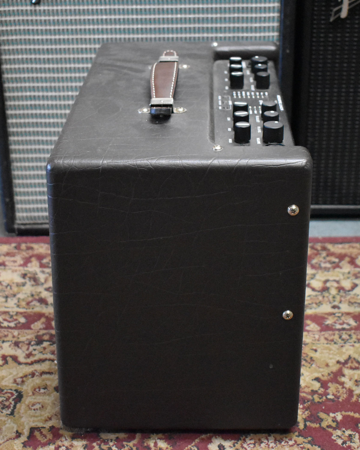 The dark brown amp is angled to show its textured top with a brown leather handle and a control panel with black knobs.