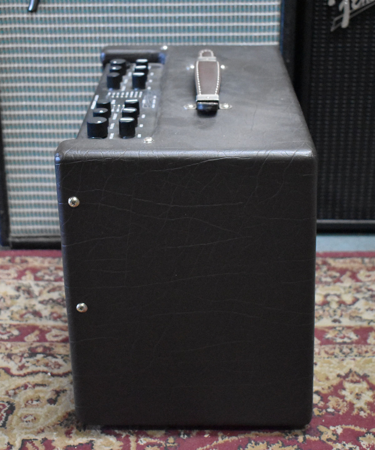 The dark brown amp is seen from the right side, showing the top panel with black controls and a brown leather handle.