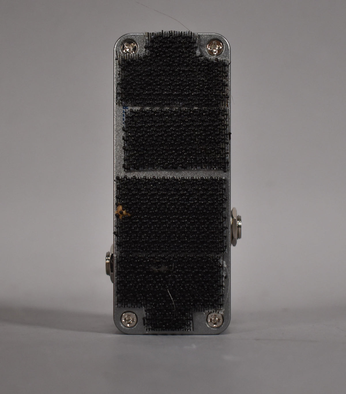 The pedal's silver bottom is covered in black hook-and-loop fastener strips, with four visible screws and some wear.