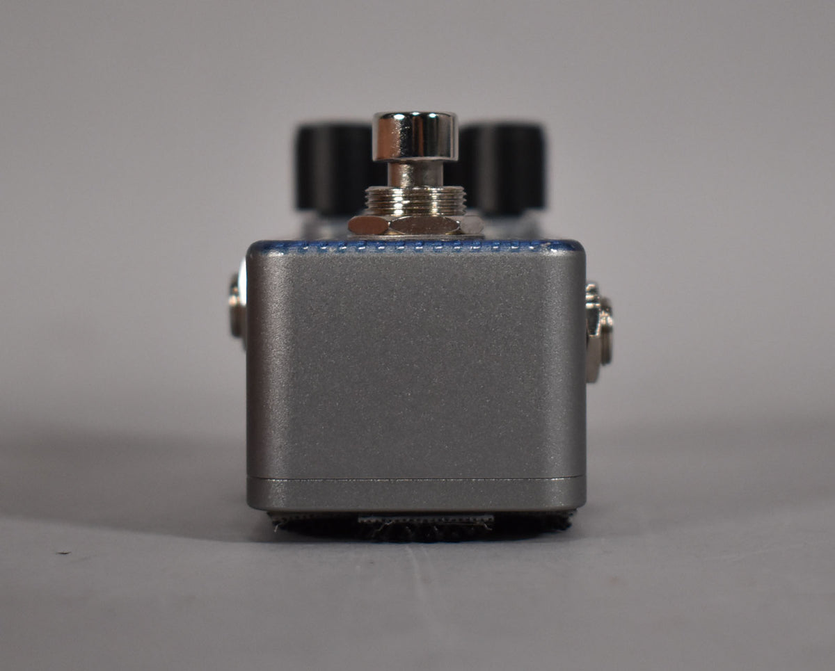 Front view of a silver guitar pedal with a chrome footswitch and two black knobs on top.