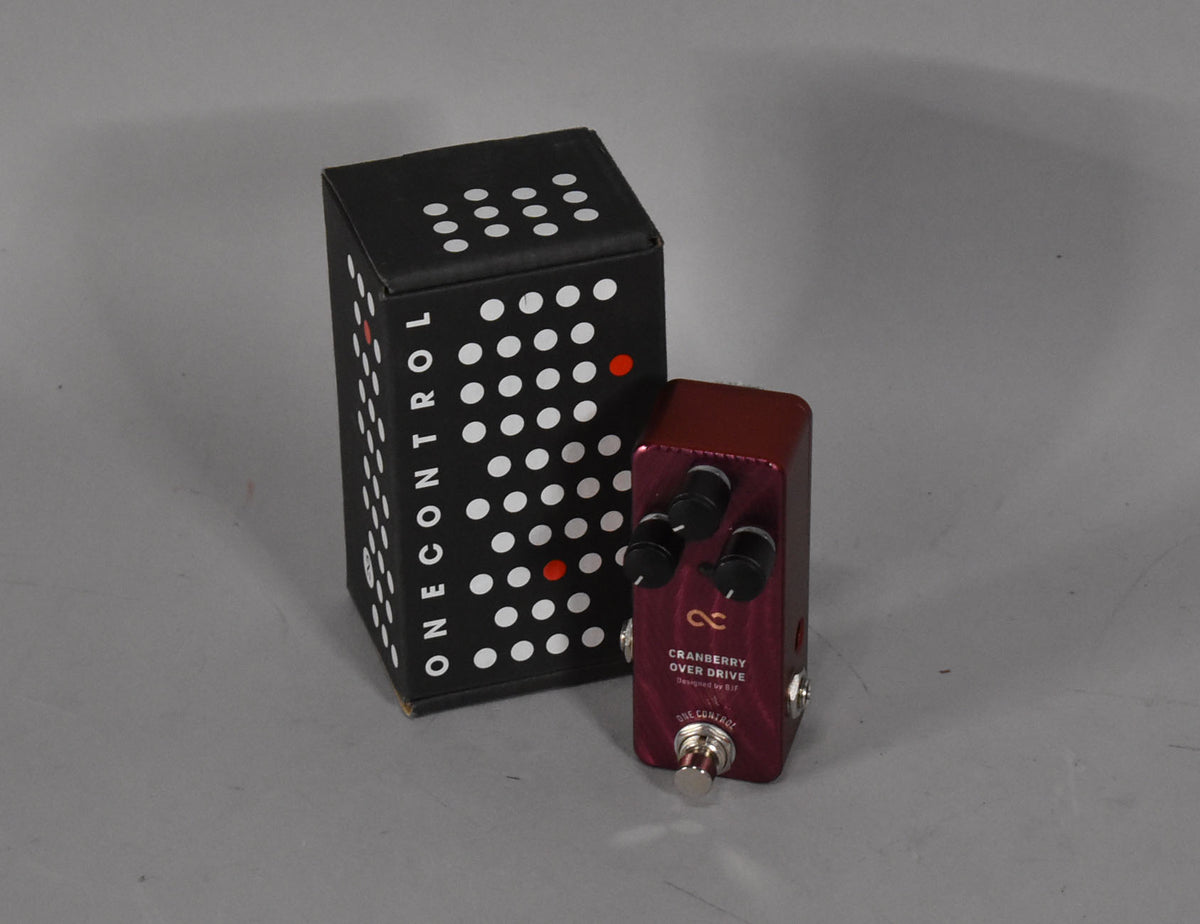 A small, metallic cranberry-red pedal with three black control knobs and a silver footswitch, next to its black box.