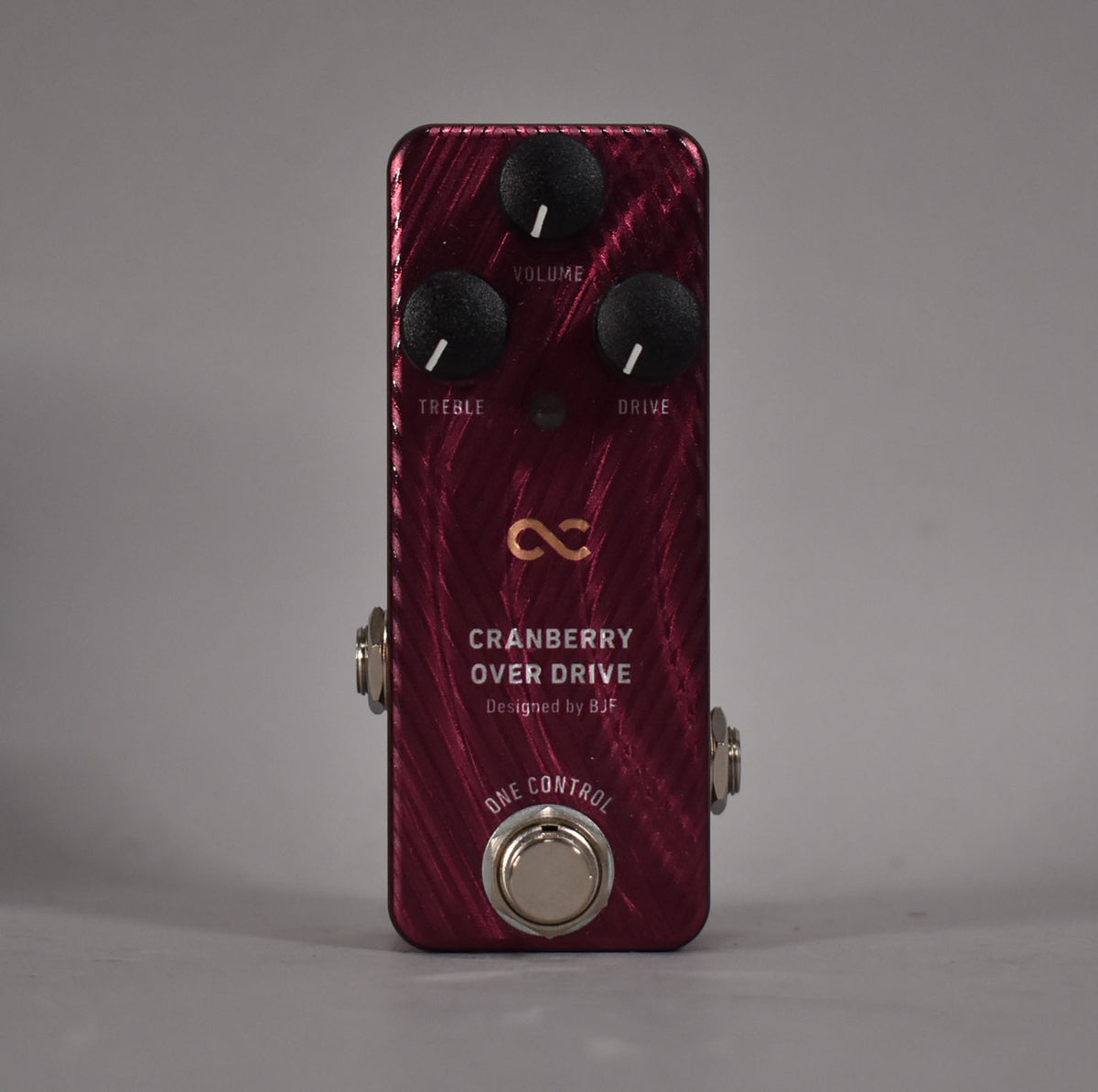 A dark red overdrive pedal with a textured finish, three black control knobs for Volume, Treble, and Drive, and a silver footswitch.