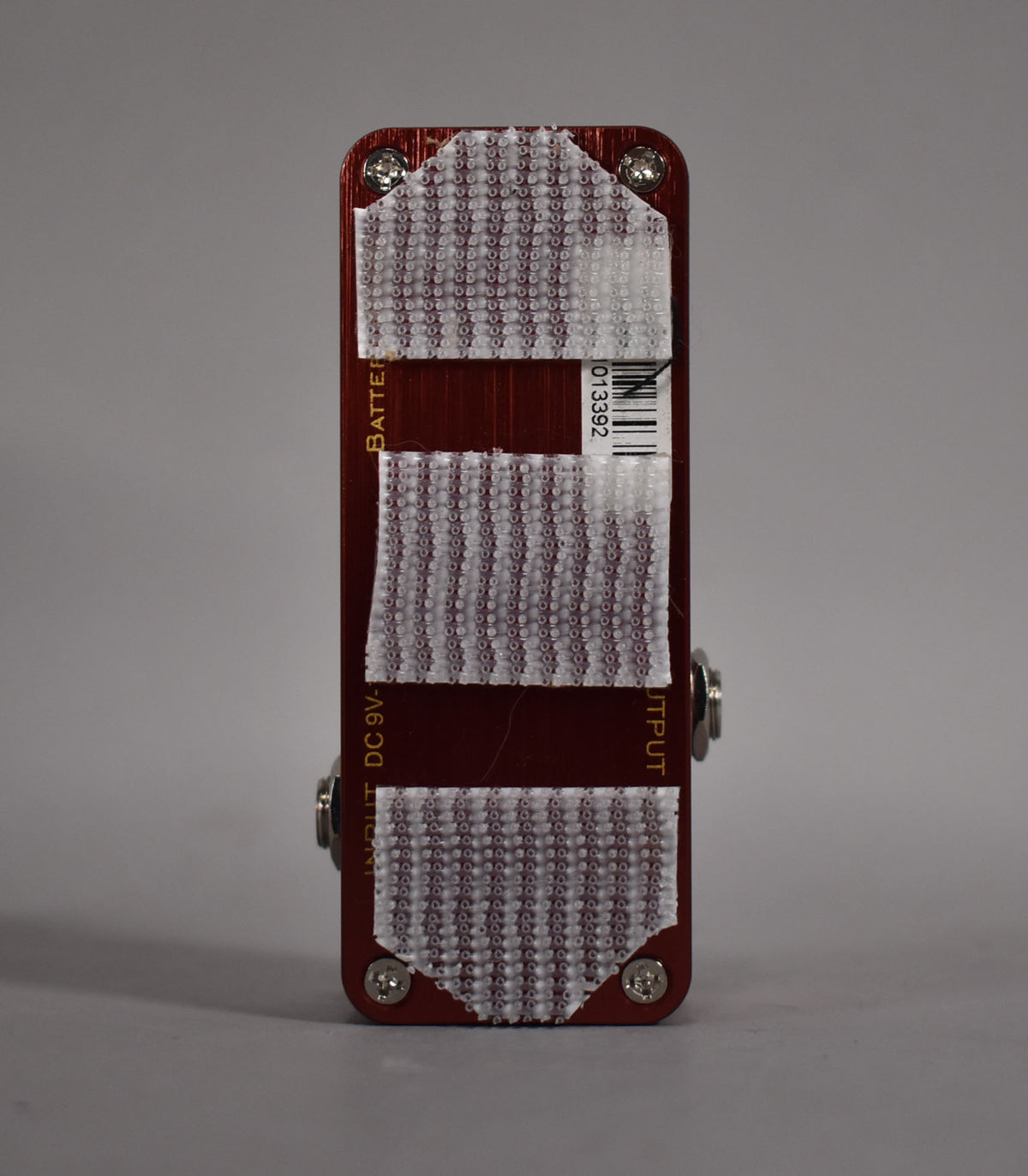The pedal's dark red bottom plate is covered with three strips of white hook-and-loop fastener and four silver screws.