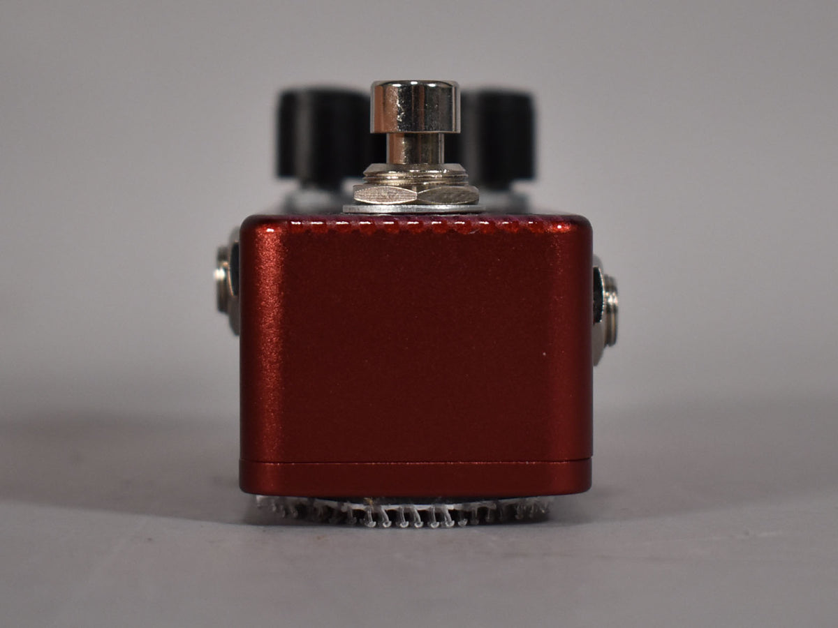 A red guitar pedal with a silver footswitch and two black knobs, viewed from the front.
