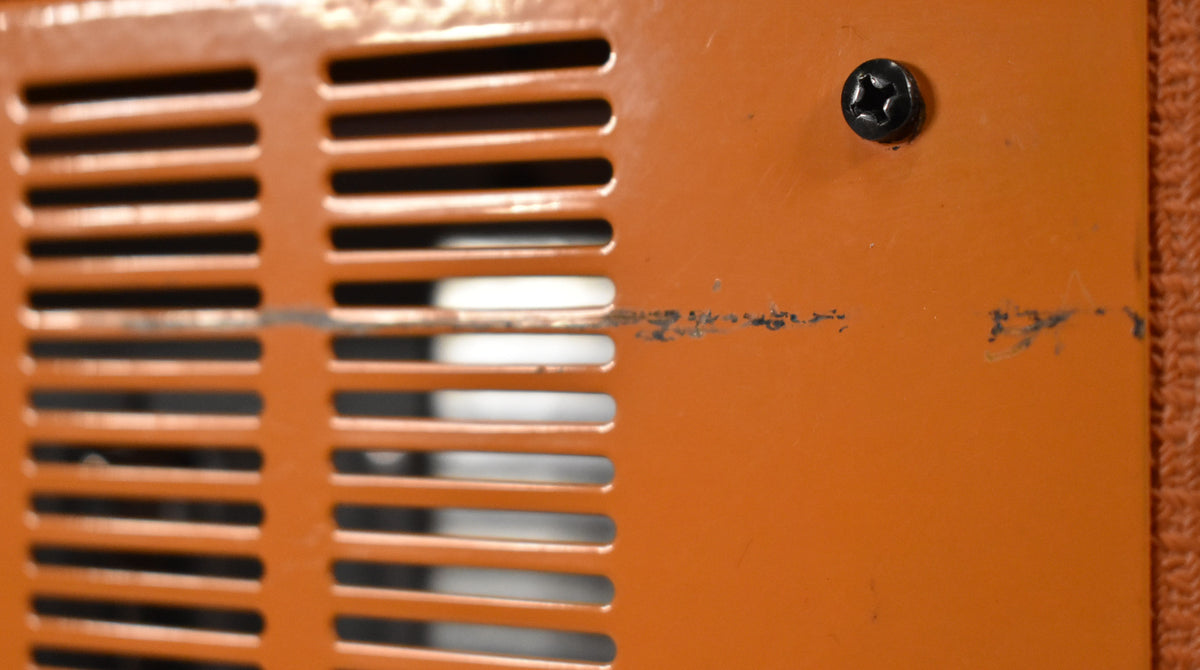 Close-up of the amp's orange metal top, showing a black screw, ventilation slats, and scuffs on the surface.