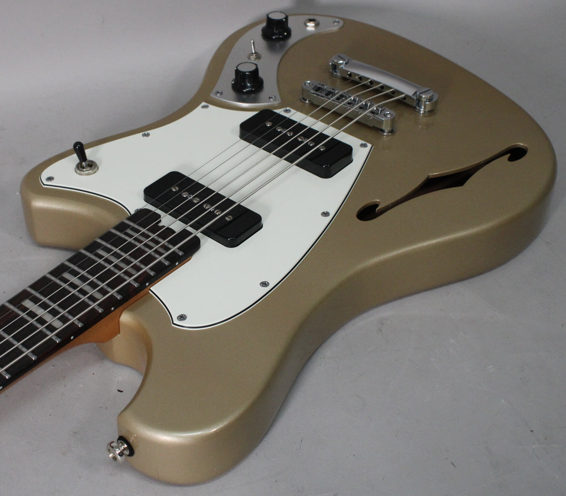 A metallic sandstone baritone guitar, angled view of the body, showing two black P90 pickups on a white pickguard and f-holes.
