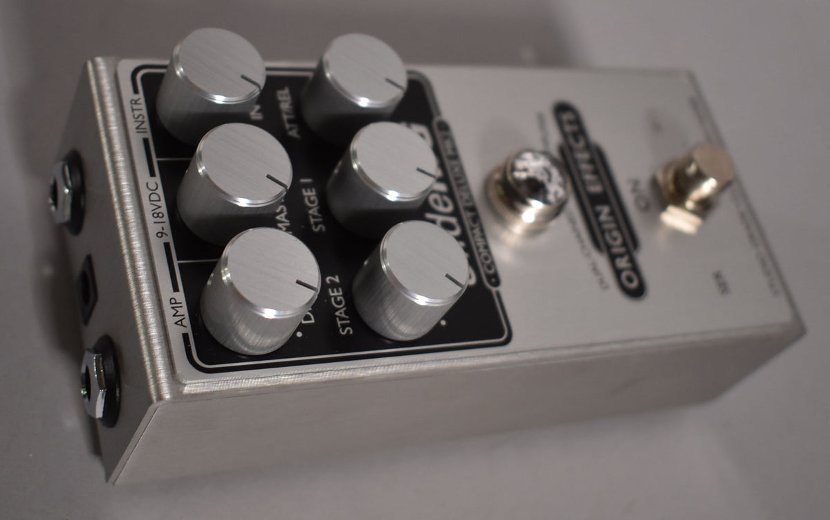 A silver Origin Effects SlideRIG Compact Deluxe Compressor MK2 pedal with six silver knobs, two footswitches, and three input jacks.
