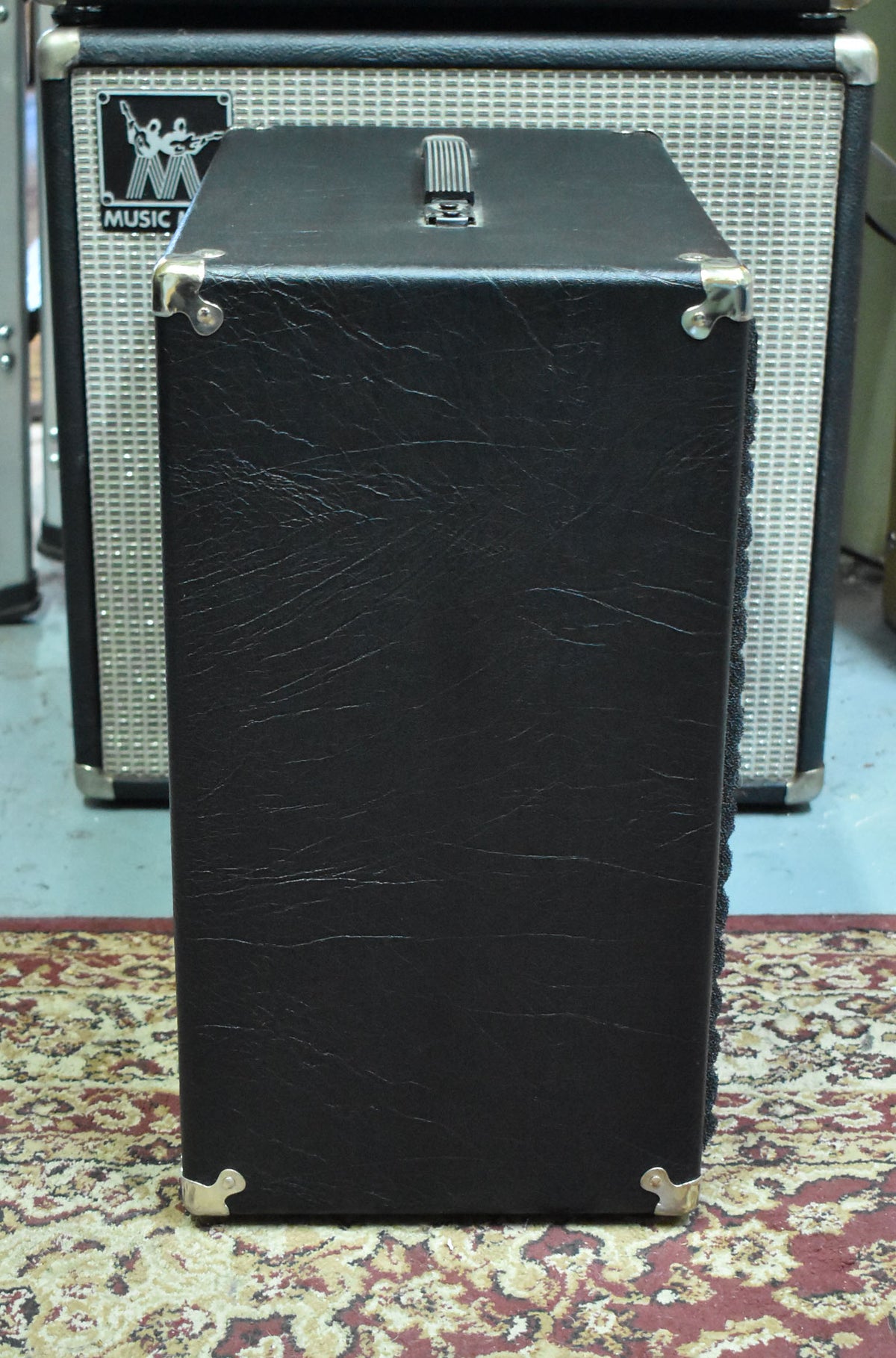 The black tolex speaker cabinet is viewed from the right side, showing a top handle and four chrome corner protectors.