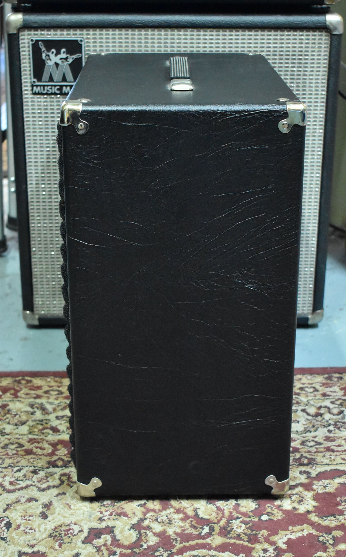 Side view of a black tolex speaker cabinet with a silver metal handle on top and four silver corner protectors.