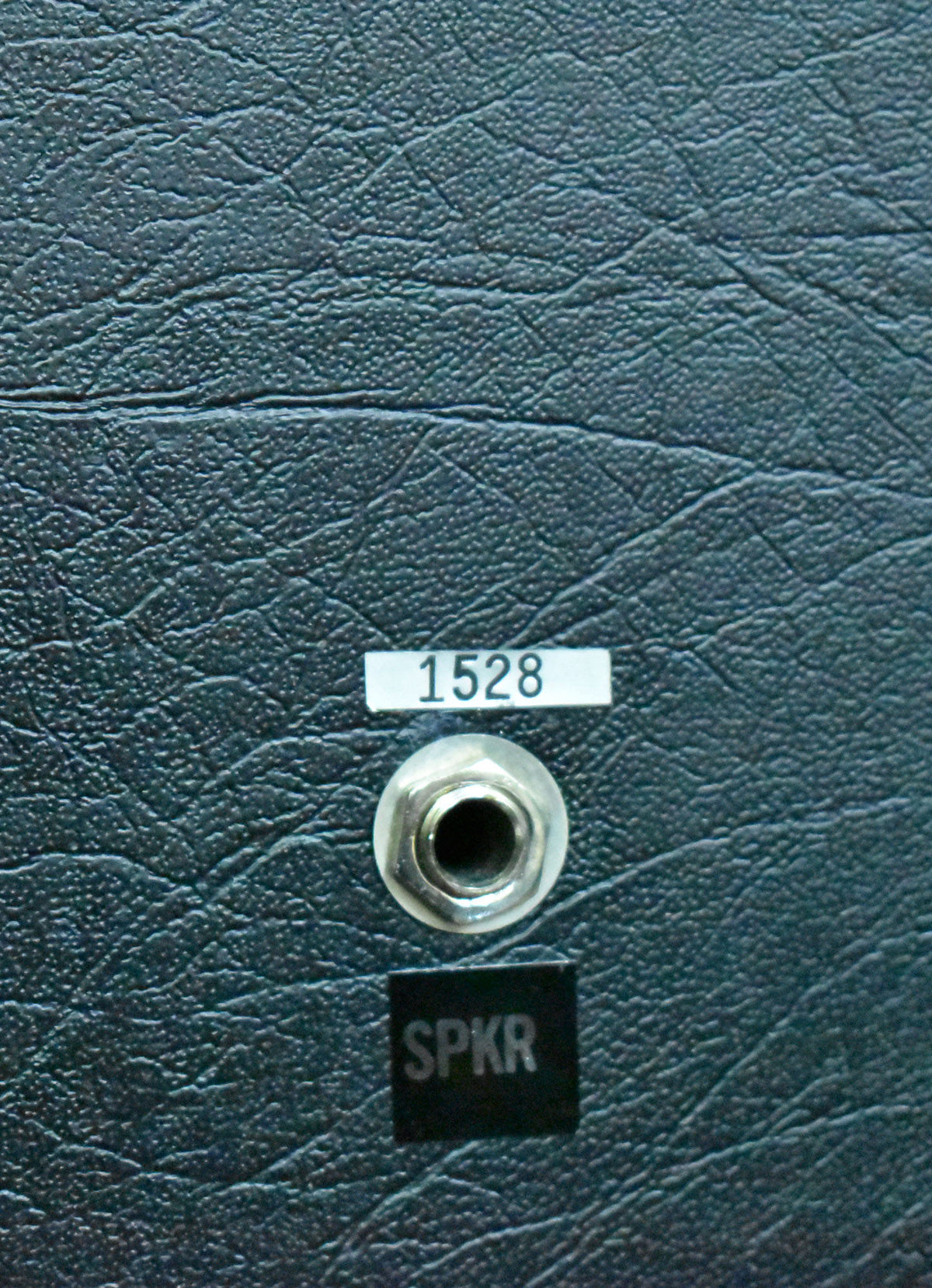 Close-up of the speaker's dark blue-green textured tolex, showing a chrome 1/4" jack with "SPKR" below and a "1528" label above.