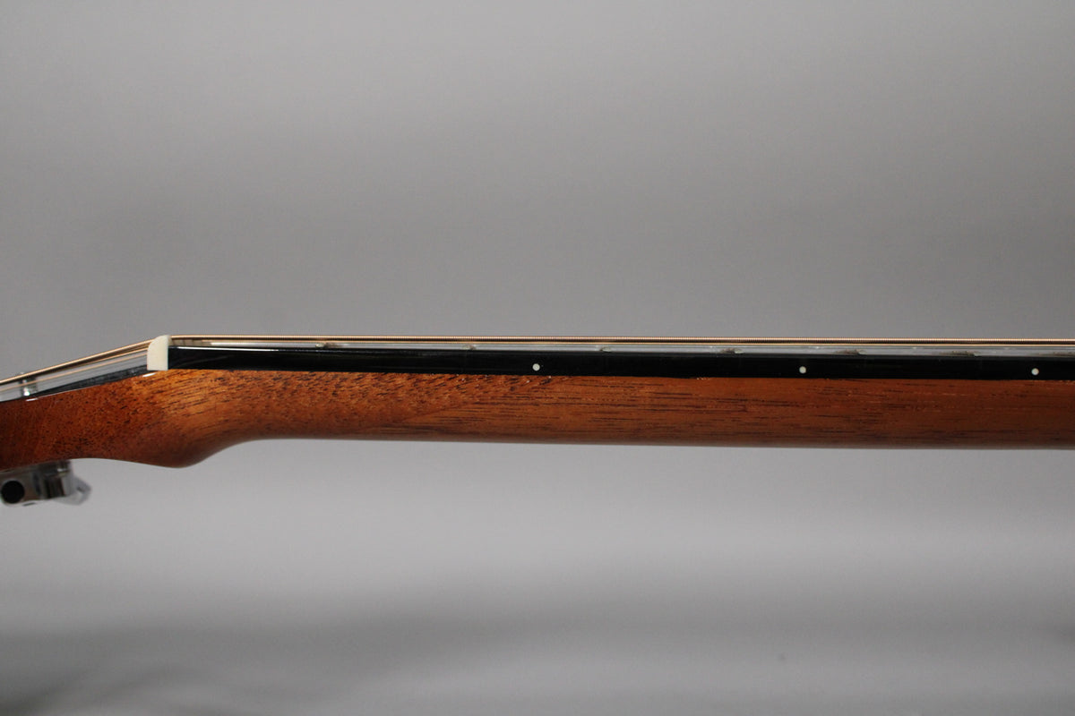The guitar's dark brown neck and fretboard are viewed from the side, showing white fret markers and a white nut.