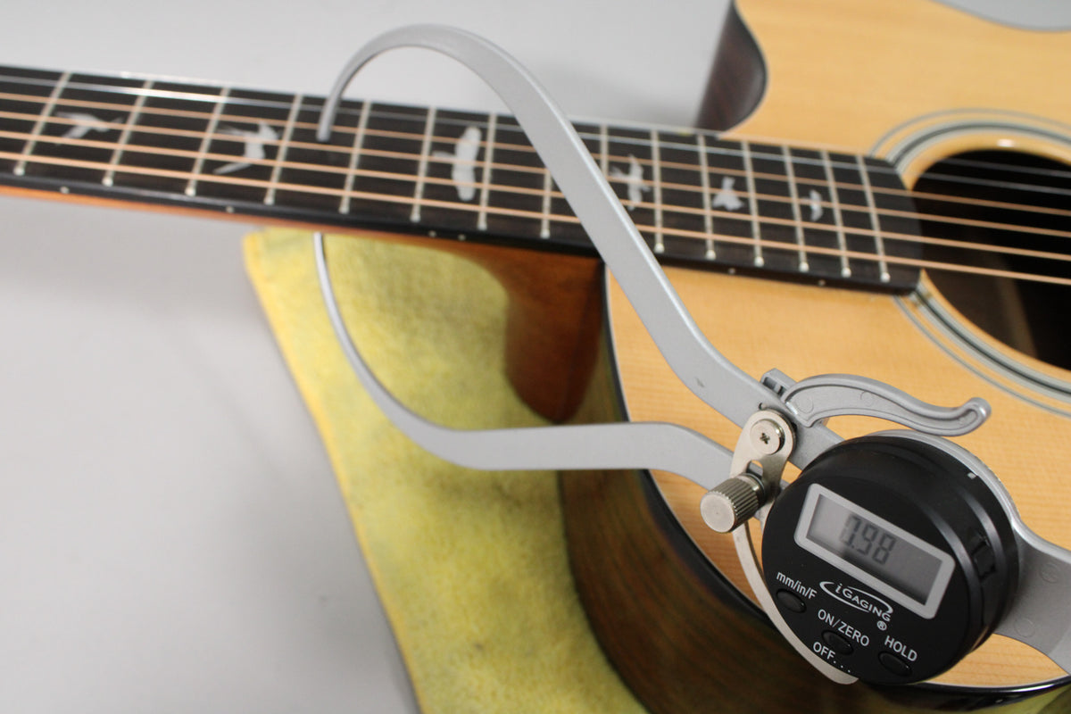 A digital caliper measures the guitar's body thickness, showing 7.98mm, with the fretboard and soundhole visible.