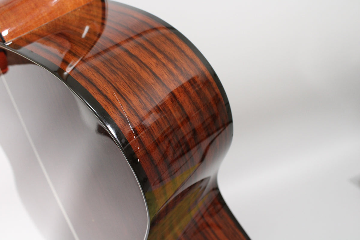 Close-up of the guitar's lower bout, showing the glossy dark brown wood grain of the side with several light scratches.