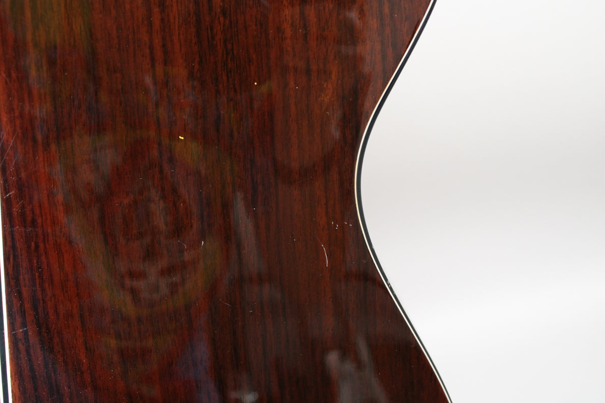 The guitar's glossy dark rosewood body, with visible grain and light surface scratches, curves into a white binding on the right.