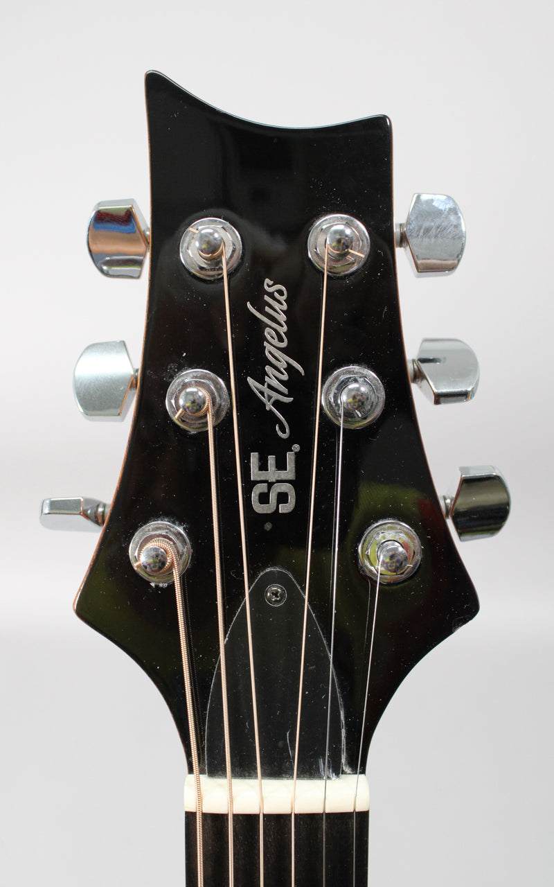 Close-up of the black gloss headstock with six chrome tuners, showing light scratches and dust.