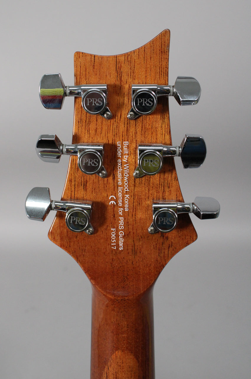 Rear view of the guitar's headstock and upper neck, showing a natural wood grain finish and six chrome tuning machines.
