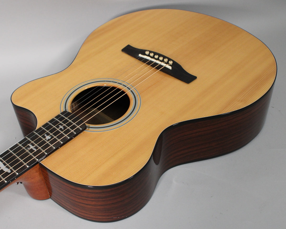 The acoustic-electric guitar's light wood top and dark rosewood sides are visible from a high angle, showing the soundhole and bridge.