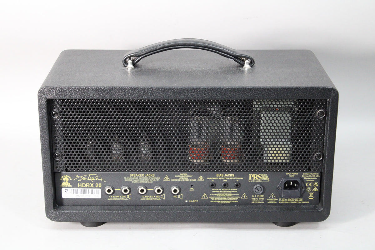 Rear view of the black tolex amp head, showing a perforated metal grille revealing glowing tubes, and various input/output jacks.